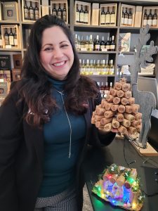 Carolina Munoz standing in the tasting bar holding a Christmas tree she made out of corks.